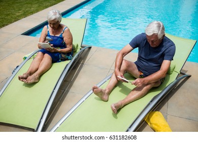 Senior couple using digital tablet on lounge chair at poolside - Powered by Shutterstock