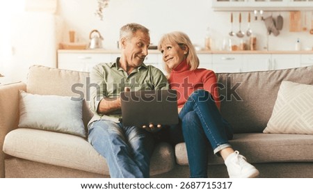 Senior Couple Using Laptop Computer Sitting On Couch At Home