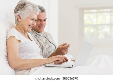 Senior couple using laptop sitting on the bed - Powered by Shutterstock