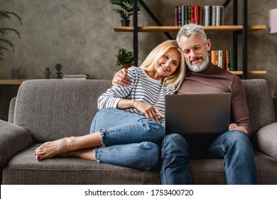 Senior couple using laptop and smiling while resting on couch at homewhile watching movie