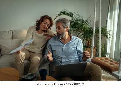 Senior couple using laptop while sitting on the sofa in the living room and going through paperwork at home - Shutterstock ID 1697989126