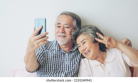 Senior Couple Using A Smart Phone Computer Face Time Call To Relatives Descendant Relatives Grandchild, Smiling Feel Happy In Bed Room Morning At Home - Lifestyle Senior Elderly Concept