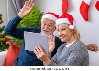 Senior couple using tablet to video phone call to greeting their family for Christmas festival, wave hand, sitting on sofa with decoration and tree - Powered by Shutterstock