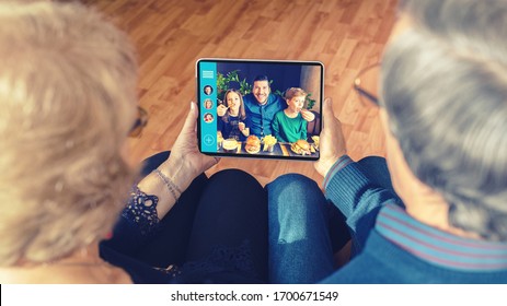 Senior couple video chatting on digital tablet with son and grandchildren due to home isolation quarantine – grandparents connecting with family on video call – old people having fun using technology - Powered by Shutterstock