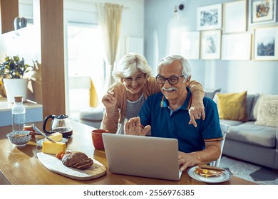 Senior couple video chatting on laptop during breakfast at home - Powered by Shutterstock