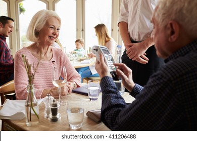 Senior Couple With Waiter Paying Bill In Restaurant