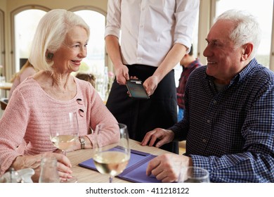 Senior Couple With Waiter Paying Bill In Restaurant