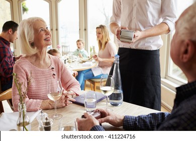 Senior Couple With Waiter Paying Bill In Restaurant