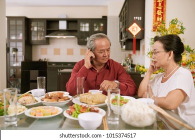 Senior couple waiting for their children and grandchildren for Chinese New Year dinner. Scrolls wishing luck and wealth in the background