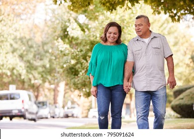Senior Couple Walking Along Suburban Street Holding Hands
