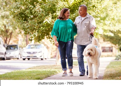 Senior Couple Walking Dog Along Suburban Street