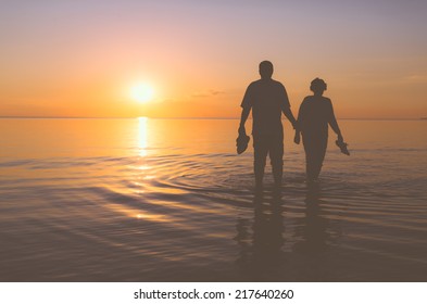 Senior couple walking holding hands in the water at sunset