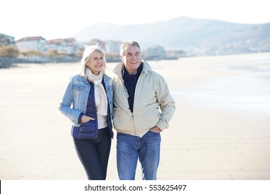 Senior Couple Walking On A Sandy Beach In Winter