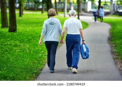 Senior couple walking outdoors at park, summertime active lifestyle. Elderly couple holding hands while walking together outdoors. Rear view of active senior couple holding hands while walking in park - Powered by Shutterstock