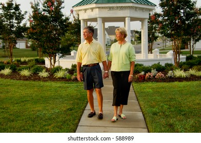 Senior Couple Walking Outside Near Garden And Gazebo