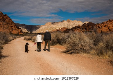 Senior Couple Walking Their Dog In The Beautiful Desert Area Of Snow Canyon State Park, Utah, USA.