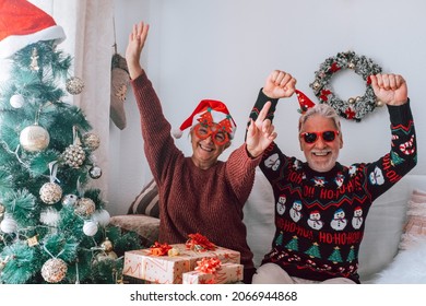 Senior Couple In Warm Clothing And Santa Hat Dancing And Celebrating In Front Of Decorated Christmas Tree At Home. Loving Old Romantic Heterosexual Couple Celebrating Christmas Festival Together