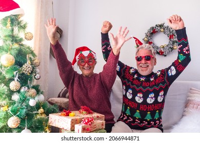 Senior Couple In Warm Clothing And Santa Hat Dancing And Celebrating In Front Of Decorated Christmas Tree At Home. Loving Old Romantic Heterosexual Couple Celebrating Christmas Festival Together