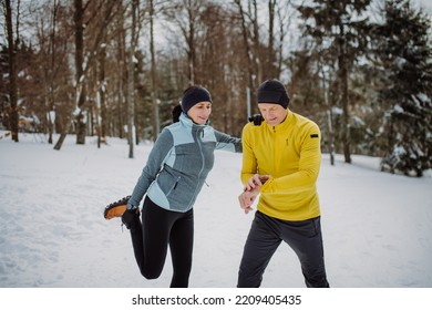 Senior couple warming-up, checking smartwatch in snowy forest before winter hike. - Powered by Shutterstock