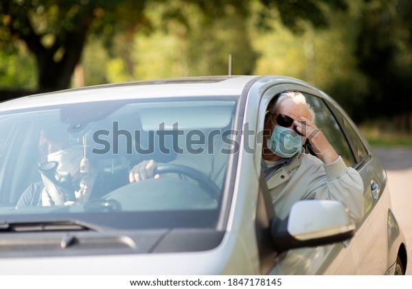 Senior couple wearing anti virus masks\
are driving in a car during the COVID-19\
pandemic