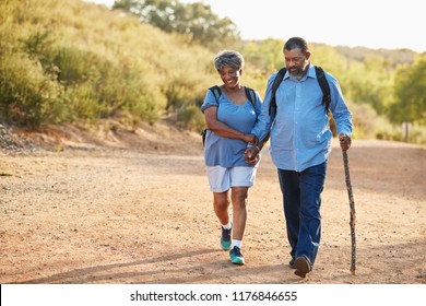 Senior Couple Wearing Backpacks Hiking In Countryside Together