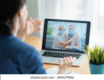 Senior couple wearing face masks and using pc for remote talking during coronavirus and flu outbreak. Virus and illness protection, home quarantine. COVID-2019.