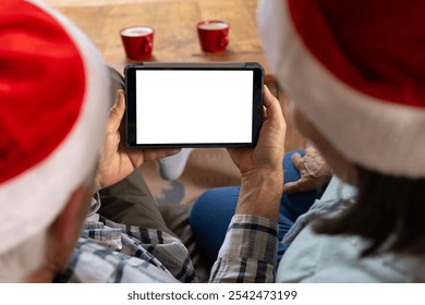 Senior couple wearing Santa hats using tablet at home during Christmas, copy space. holiday, festive, celebration, technology, elderly, together - Powered by Shutterstock