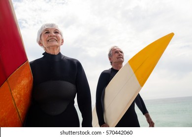 Senior couple in wetsuit holding surfboard on beach on a sunny day - Powered by Shutterstock