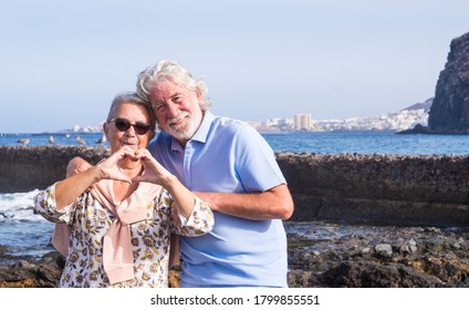 Senior couple with white hairs hugging at the beach making heart shape with hands - horizon over water and city - concept of active seniors during holidays - Powered by Shutterstock