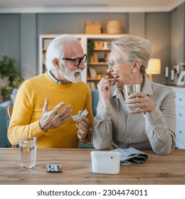 Senior couple woman take medicine or supplement vitamin treatment cure while her husband old caucasian man sit beside at the table at home real people family old people retirement and health concept - Powered by Shutterstock