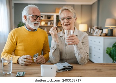 Senior couple woman take medicine or supplement vitamin treatment cure while her husband old caucasian man sit beside at the table at home real people family old people retirement and health concept - Powered by Shutterstock