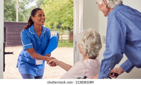 Senior Couple With Woman In Wheelchair Greeting Nurse Or Care Worker Making Home Visit At Door