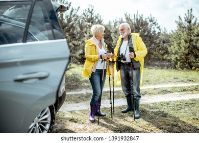 Senior couple in yellow raincoats standing near the car in the forest, enjoying their retirement - Shutterstock ID 1391932847