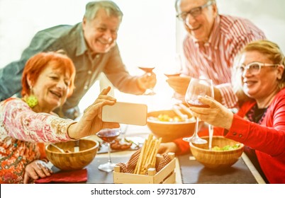 Senior couples taking selfie at home toasting red wine and eating lunch meal - Old friends having fun with new trends technology - Joyful elderly  lifestyle concept - Focus on phone hand - Warm filter - Powered by Shutterstock