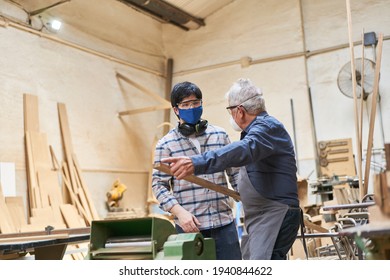 Senior Craftsman And Apprentice In Training In Workshop With Face Mask Due To Covid-19 And Coronavirus Pandemic