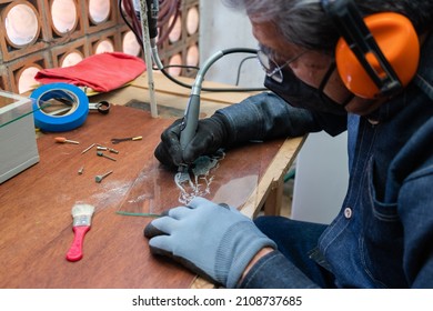 A senior craftsman wearing personal protective equipment does glass engraving with a rotary tool