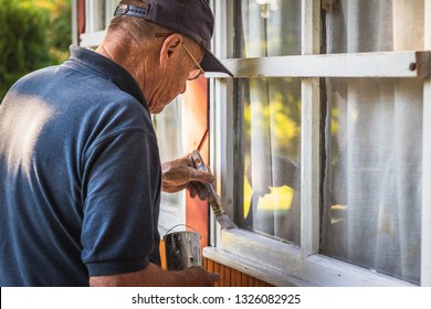 Senior Craftsperson Is Painting House Exterior. Home Improvement. Old Man Repairing Window Frame.