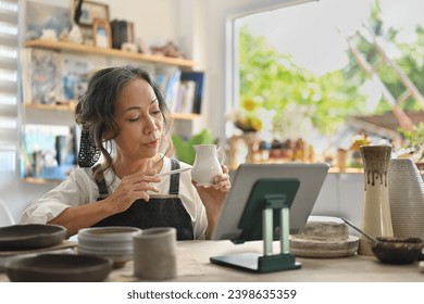 Senior craftswoman selling ceramic on the online platform with digital tablet in the art store, Small Business, and Crockery Shop concepts. - Powered by Shutterstock