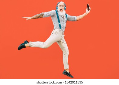 Senior crazy man jumping while listening music outdoor - Hipster male having fun dancing and celebrating life outside - Happiness, technology and elderly lifestyle people concept