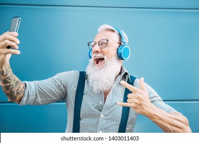 Senior Crazy Man Taking Self Video While Listening Music With Headphones - Hipster Guy Having Fun Using Mobile Smartphone Playlist Apps - Happiness, Technology And Elderly Lifestyle People Concept