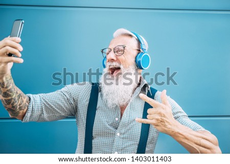 Senior crazy man taking self video while listening music with headphones - Hipster guy having fun using mobile smartphone playlist apps - Happiness, technology and elderly lifestyle people concept