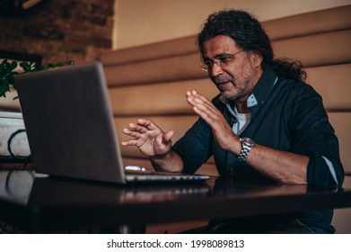Senior cuban man using his laptop for an online video call while sitting in a cafe