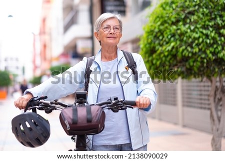 Senior cyclist woman pushing her electric bicycle in urban street looking ahead. Active elderly grandmother enjoying a healthy lifestyle and freedom