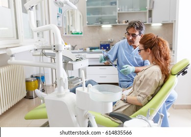 Senior  Dentist In Dental Office Talking With Female Patient And Preparing For Treatment.