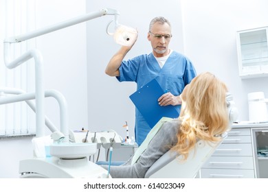 Senior Dentist In Uniform Talking With Patient In Dental Clinic 