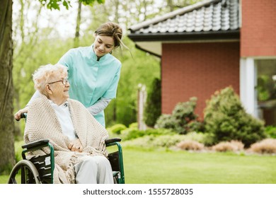 Senior Disabled Woman With Caregiver In The Garden Of The Nursing Home