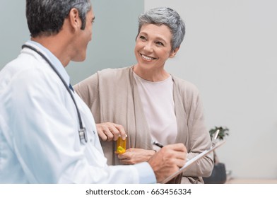 Senior doctor in conversation with senior woman holding medicine box. General practitioner and patient discussing at office. Happy doctor discussing with patient and prescribes pills.