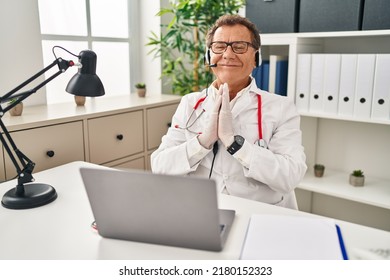 Senior Doctor Man Working On Online Appointment Praying With Hands Together Asking For Forgiveness Smiling Confident. 