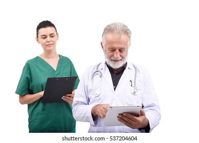 Senior Doctor And A Nurse Smiling At The Information They Are Reviewing On A Clipboard. Multiracial Team Of Doctors Discussing A Patient. Medical Professionals In A Discussion.