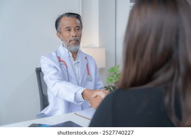 Senior doctor shaking hands with a patient in a clinic, showing trust and care in healthcare - Powered by Shutterstock